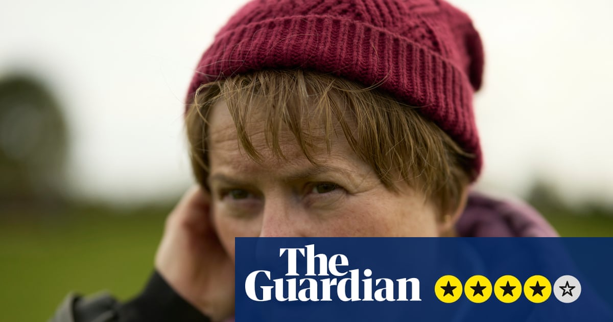 Monica Dolan, as Catherine Corless, touches her ear with a concerned expression outdoors